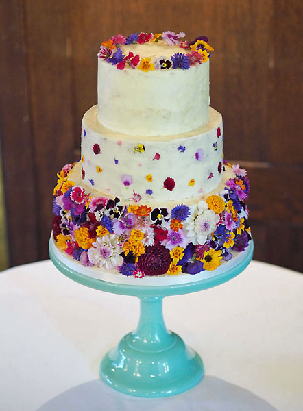 A 'Colour Burst' of Fresh Wild Summer Edible Flowers, covering a Buttercream Iced Wedding Cake, Topped with a Crown.